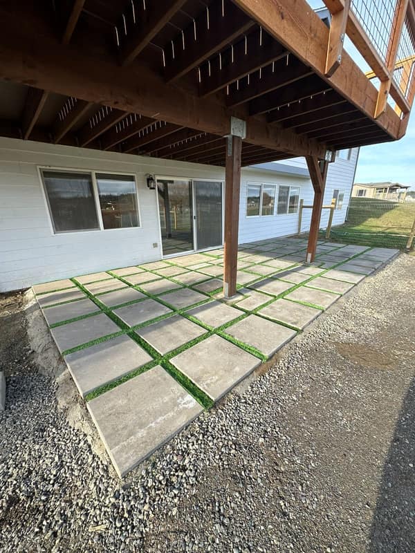 Custom paver patio with grass-filled joints set beneath a residential deck — Olympic Peninsula
